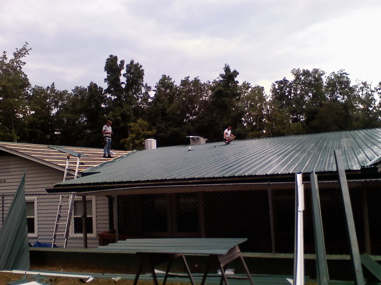 Two roofers installing green metal panels above a covered porch in Springfield